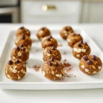 Für diese leckeren Energie-Bällchen brauchst du einfache und gesunde Zutaten. Hier ist die Liste: - 1 Tasse Haferflocken (gerollt) - ½ Tasse Kürbispüree - ¼ Tasse Mandelbutter (oder eine Nussbutter deiner Wahl) - ¼ Tasse Honig oder Ahornsirup - 2 Esslöffel ungesüßtes Kakaopulver - 1 Esslöffel Instantkaffeegranulat - 1 Teelöffel Vanilleextrakt - ½ Teelöffel Zimt - Eine Prise Salz - ¼ Tasse Mini-Schokoladenstückchen (optional) - ¼ Tasse gehackte Nüsse oder Samen (optional) Diese Zutaten bieten eine tolle Kombination aus Geschmack und Nährstoffen. Haferflocken liefern Ballaststoffe und Energie. Kürbispüree bringt Vitamine und Feuchtigkeit. Mandelbutter fügt gesunde Fette und Proteine hinzu. Honig oder Ahornsirup süßen die Mischung auf natürliche Weise. Du kannst die Zutaten leicht anpassen, um deinen eigenen Twist hinzuzufügen. Wenn du keine Mandelbutter magst, probiere Erdnussbutter oder Sonnenblumenbutter. Du kannst auch verschiedene Süßungsmittel verwenden, wie Kokosblütenzucker oder Dattelsirup. Möchtest du mehr Crunch? Füge eine Handvoll gehackte Nüsse oder Samen hinzu. Für extra Schokoladengeschmack kannst du mehr Kakaopulver oder Schokoladenstückchen verwenden. Sei kreativ und finde die Kombination, die dir am besten schmeckt. Jede Zutat hat ihre eigenen Vorteile. Haferflocken sind reich an Ballaststoffen. Sie helfen dir, länger satt zu bleiben. Kürbispüree ist eine großartige Quelle für Vitamin A und Antioxidantien. Mandelbutter liefert gesunde Fette, die gut für dein Herz sind. Kakaopulver enthält Flavonoide, die gut für die Gesundheit sind. Instantkaffee gibt dir einen kleinen Energieschub, ohne viel Koffein. Zimt kann den Blutzuckerspiegel stabilisieren. Diese Zutaten machen die Bällchen nicht nur lecker, sondern auch nahrhaft. Um die No Bake Mocha Pumpkin Energy Bites zu machen, beginne mit einer großen Schüssel. Mische 1 Tasse Haferflocken, ½ Tasse Kürbispüree, ¼ Tasse Mandelbutter und ¼ Tasse Honig. Rühre gut, bis alles verbunden ist. Füge 2 Esslöffel Kakaopulver, 1 Esslöffel Instantkaffeegranulat, 1 Teelöffel Vanilleextrakt, ½ Teelöffel Zimt und eine Prise Salz hinzu. Mische weiter, bis die Masse gleichmäßig ist. Wenn du magst, gib die optionalen Zutaten wie Mini-Schokoladenstückchen und Nüsse dazu. Nachdem alles gut vermischt ist, stelle die Schüssel für 15-20 Minuten in den Kühlschrank. So wird die Mischung fester und leichter zu formen. Die Konsistenz ist wichtig für die Formung der Bällchen. Wenn die Mischung zu trocken ist, füge etwas mehr Kürbispüree oder Mandelbutter hinzu. Ist sie zu feucht, gib etwas mehr Haferflocken oder Kakaopulver hinzu. Achte darauf, dass die Mischung gut zusammenhält. Ein guter Trick ist, die Mischung vor dem Formen zu kühlen. So bleibt sie stabiler. Nimm die gekühlte Mischung aus dem Kühlschrank und forme mit deinen Händen kleine Bällchen, etwa 2,5 cm groß. Achte darauf, dass die Bällchen gleichmäßig sind, damit sie gut aussehen. Lege sie auf ein mit Backpapier ausgelegtes Blech. Du kannst die Bällchen sofort essen oder für eine festere Textur eine Stunde kühlen. Bewahre die übrig gebliebenen Bällchen in einem luftdichten Behälter im Kühlschrank auf. So bleiben sie frisch bis zu einer Woche. Ein häufiges Problem ist, dass die Mischung zu trocken ist. Das passiert, wenn du nicht genug Kürbispüree oder Nussbutter hinzufügst. Achte darauf, die Zutaten gut zu mischen. Wenn die Masse bröckelig ist, füge einen Esslöffel Wasser hinzu. Wenn die Mischung zu feucht ist, gib mehr Haferflocken dazu. So bekommst du die richtige Konsistenz für die Bällchen. Der Kühlschrankzeitraum ist wichtig. Lass die Mischung für 15 bis 20 Minuten kühlen. So wird sie fester und leichter zu formen. Wenn du die Bällchen noch fester magst, lege sie eine Stunde in den Kühlschrank. Das macht sie perfekt zum Snacken. Präsentiere die Bällchen auf einem schönen Teller. Du kannst sie mit zusätzlichen Schokoladenstückchen oder einer Prise Zimt garnieren. Das sieht nicht nur gut aus, sondern macht die Bällchen auch noch leckerer. Für einen besonderen Touch, serviere sie mit einer Tasse Kaffee oder Tee. {{image_4}} Wenn du keine Mandelbutter magst, gibt es tolle Alternativen. Erdnussbutter ist eine beliebte Wahl. Sie verleiht den Bällchen einen süßen Geschmack. Sonnenblumenbutter ist eine gute Option für Allergiker. Sie hat einen milden Geschmack und ist nussfrei. Cashewbutter bietet eine cremige Textur und einen sanften Geschmack. Probiere verschiedene Nussbutter aus, um deine perfekte Kombination zu finden. Du kannst die No Bake Mocha Pumpkin Energy Bites mit weiteren Aromen aufpeppen. Füge einen Löffel Kokosnussraspeln für einen tropischen Touch hinzu. Ein bisschen Muskatnuss gibt den Bällchen eine warme Note. Für Schokoladenfans sind Kakaonibs eine großartige Ergänzung. Wenn du es scharf magst, probiere etwas Ingwerpulver. Sei kreativ und passe die Bällchen deinem Geschmack an! Für vegane Bällchen, ersetze Honig durch Ahornsirup oder Agavendicksaft. Diese Süßstoffe sind pflanzlich und lecker. Achte darauf, glutenfreie Haferflocken zu verwenden, um die Bällchen glutenfrei zu machen. So kannst du die Energie-Bällchen für alle geeignet machen. Mit diesen Anpassungen bleiben sie nahrhaft und schmackhaft. Um die No Bake Mocha Pumpkin Energy Bites frisch zu halten, lagere sie in einem luftdichten Behälter. Dies schützt sie vor Feuchtigkeit und Gerüchen. Der Kühlschrank ist der beste Ort dafür. Stelle sicher, dass der Behälter gut verschlossen ist. So bleiben die Bällchen länger lecker und nahrhaft. Im Kühlschrank halten die Energie-Bällchen bis zu einer Woche. Nach ein paar Tagen können sie etwas weicher werden, aber sie sind trotzdem köstlich. Achte darauf, sie nicht zu lange stehen zu lassen, um die besten Aromen zu genießen. Am besten isst du sie frisch, aber sie sind auch nach ein paar Tagen noch gut. Wenn du die Bällchen länger aufbewahren möchtest, kannst du sie einfrieren. Lege sie auf ein Backblech und friere sie für etwa eine Stunde ein. Danach packe die Bällchen in einen luftdichten Gefrierbeutel. So bleiben sie bis zu drei Monate frisch. Wenn du Lust auf einen Snack hast, nimm einfach ein paar Bällchen heraus und lasse sie bei Raumtemperatur auftauen. So hast du immer eine gesunde Leckerei zur Hand. Ja, du kannst die Bällchen ohne Koffein machen. Lass einfach das Instantkaffeegranulat weg. Du kannst auch einen anderen Geschmack hinzufügen. Zum Beispiel, nutze mehr Zimt oder Vanille. Das gibt den Bällchen einen tollen Geschmack ohne Koffein. Es gibt viele Optionen, um die Bällchen süßer zu machen. Honig ist eine gute Wahl, weil er natürlich ist. Ahornsirup funktioniert auch gut. Wenn du weniger Zucker willst, versuche Datteln oder Bananen. Diese geben eine natürliche Süße und machen die Bällchen weich und klebrig. Die Bällchen halten sich bis zu einer Woche im Kühlschrank. Achte darauf, sie in einem luftdichten Behälter zu lagern. Wenn du sie länger aufbewahren willst, kannst du sie auch einfrieren. So bleiben sie frisch und lecker für bis zu drei Monate. Die No-Bake Mocha Pumpkin Energy Bites sind einfach und schnell zuzubereiten. Wir haben die wichtigsten Zutaten, die Zubereitung und viele Tipps besprochen. Es ist wichtig, die richtige Konsistenz zu finden und häufige Fehler zu vermeiden. Variationen wie verschiedene Nussbutter oder zusätzliche Geschmäcker machen die Bällchen noch besser. Achte auf die Lagerung, damit sie frisch bleiben. Probiere neue Kombinationen aus und finde deinen Favoriten! Genieß deine gesunden Snacks oder teile sie mit Freunden.